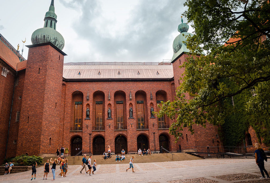 People walking, sitting, and taking picture outside the red-bricked City Hall building