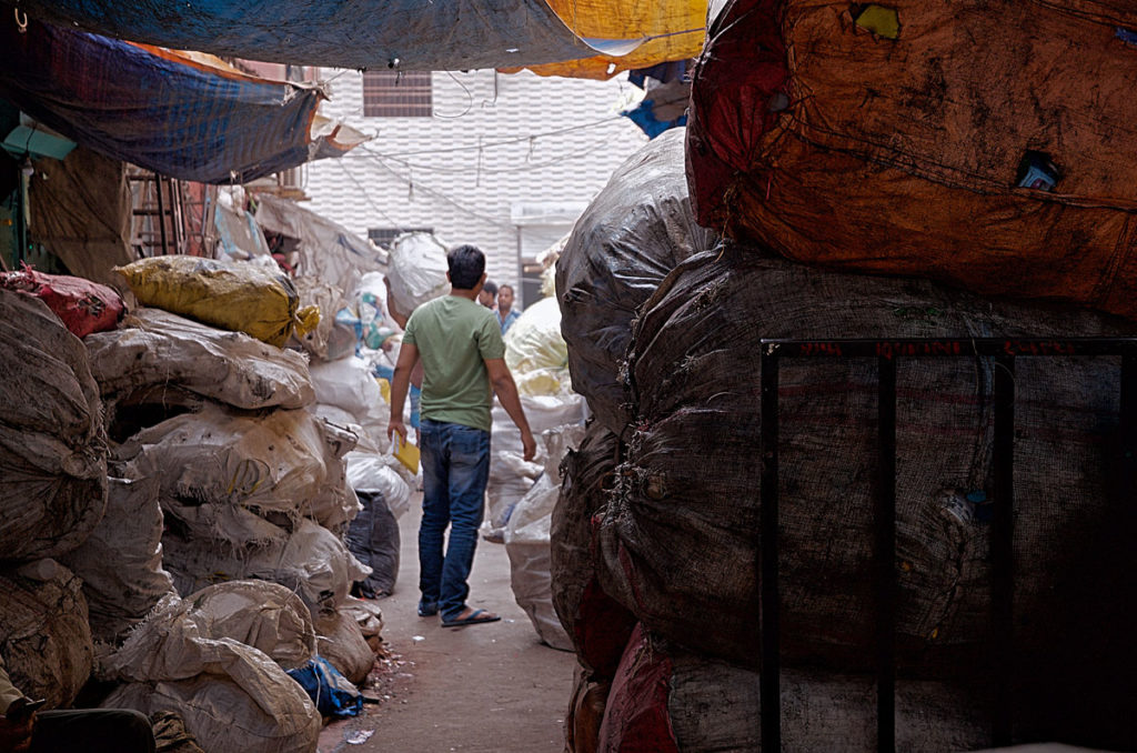 Men between stacks of recyclable junk items - Dharavi
