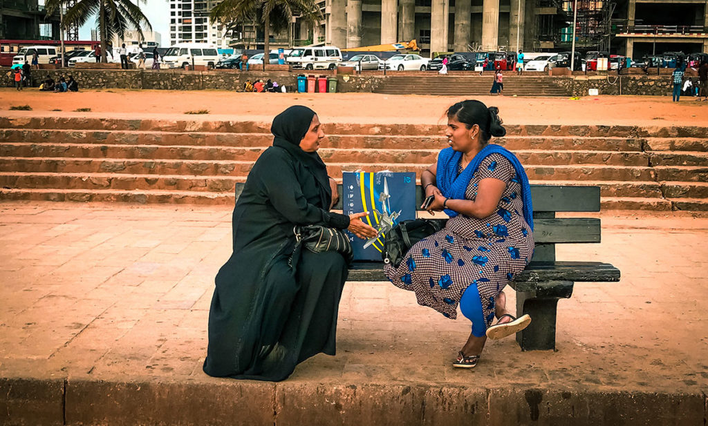 Two women sitting on a beach talking - Colombo
