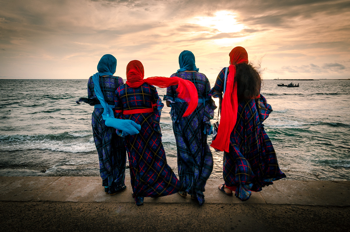 Four women with scarves facings the beach