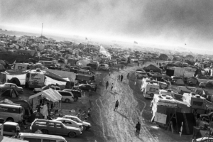 Burning Man attendees walking the desert road surrounded by parked cars and tents